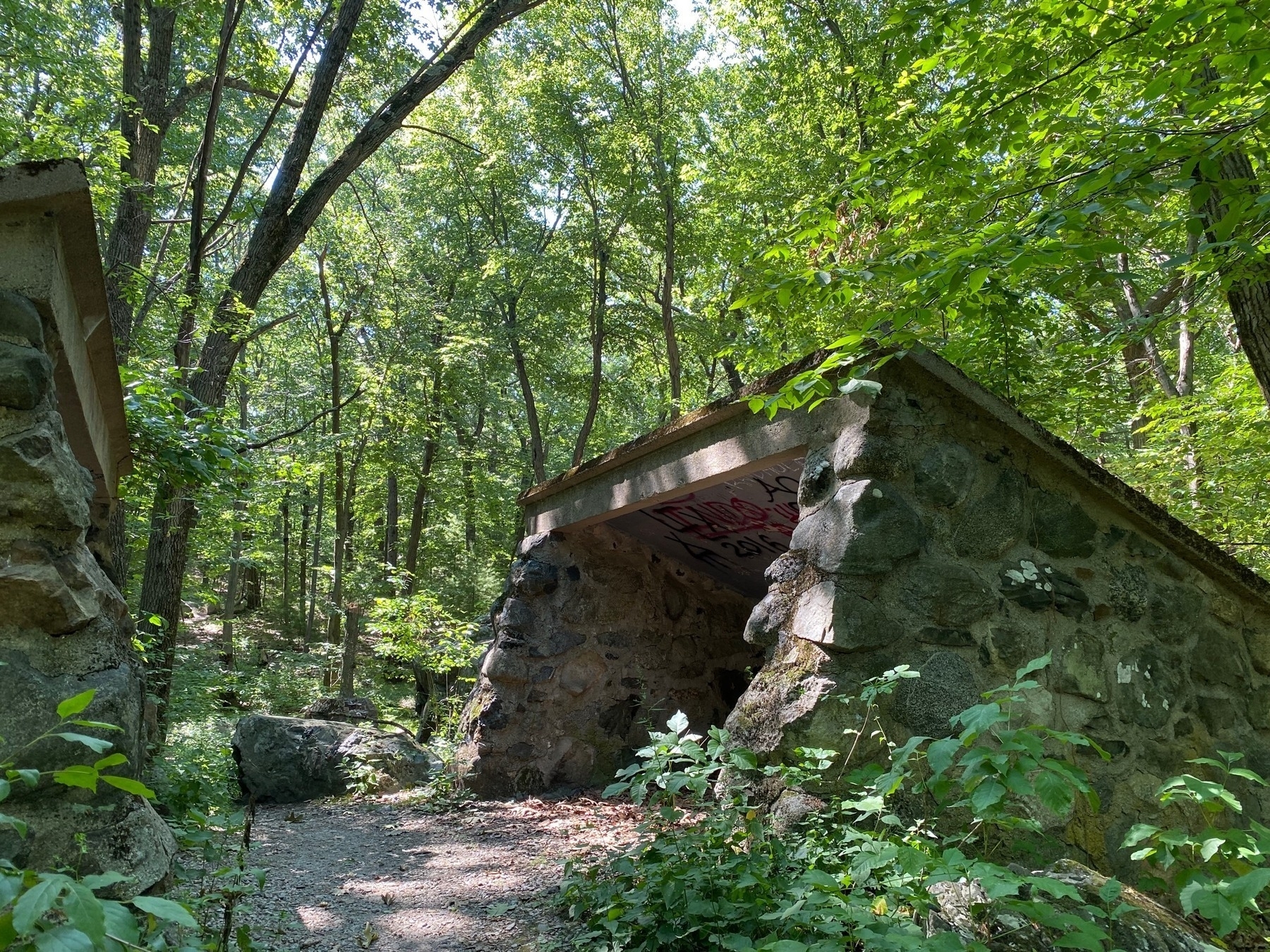 View of a small stone structure surrounded by sunlit trees.