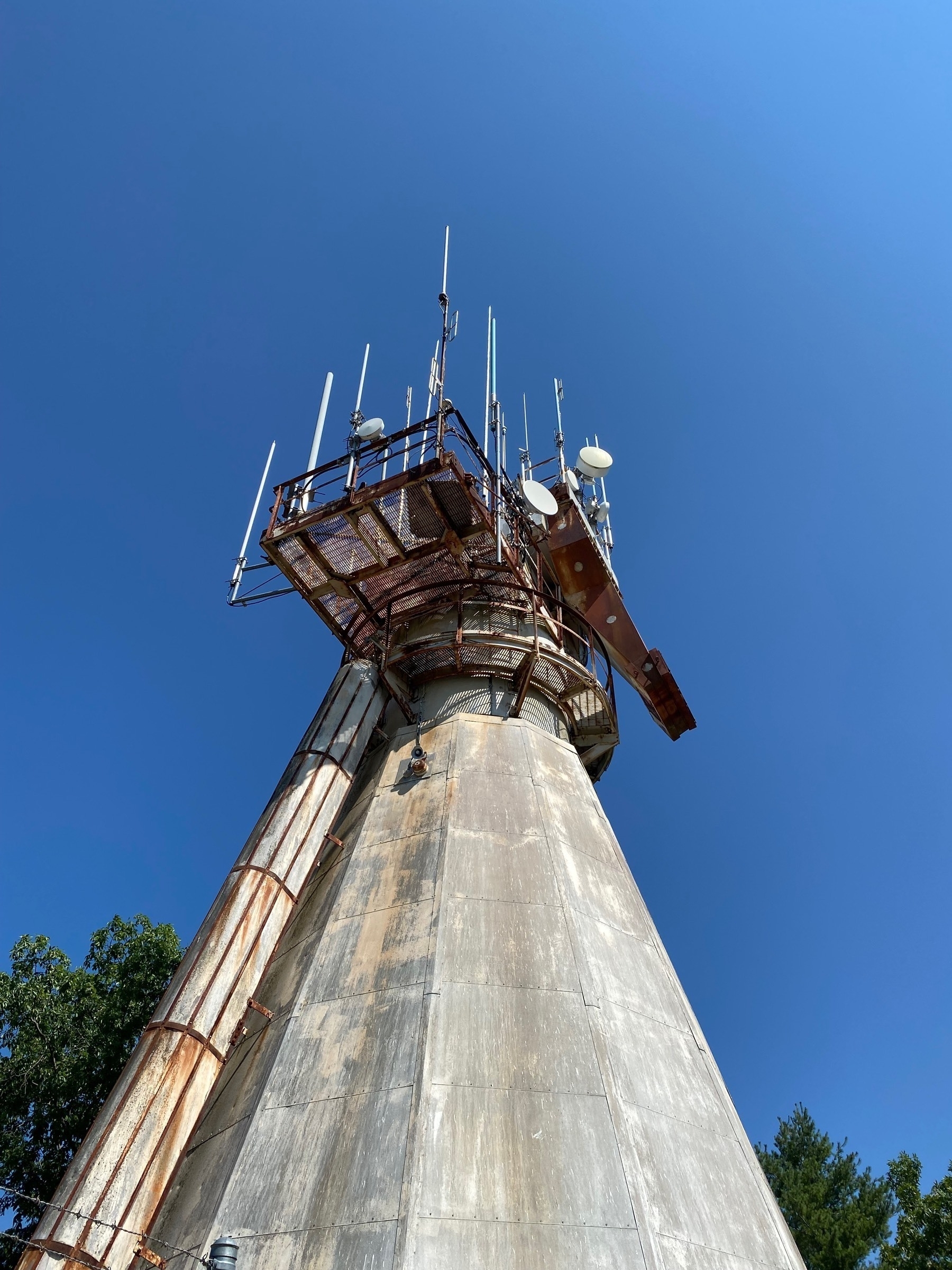 View up towards a cement tower with gantries and antennas at the top.