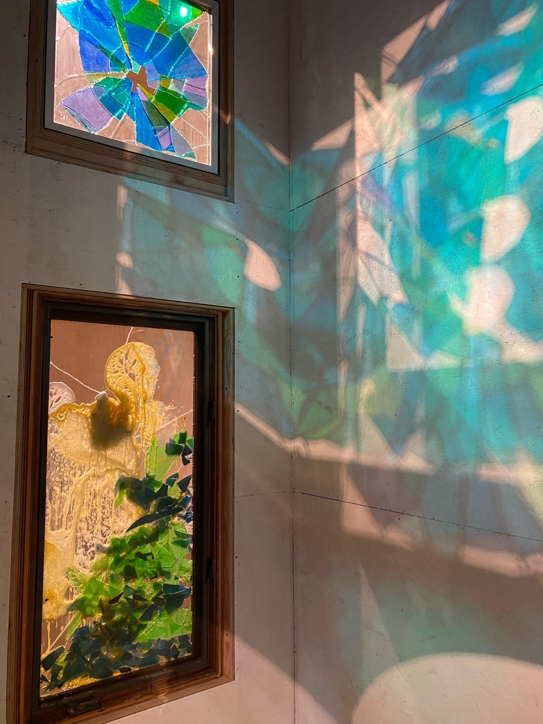 Stained glass windows on the left, with a light shining behind them and casting colored patterns on the right.