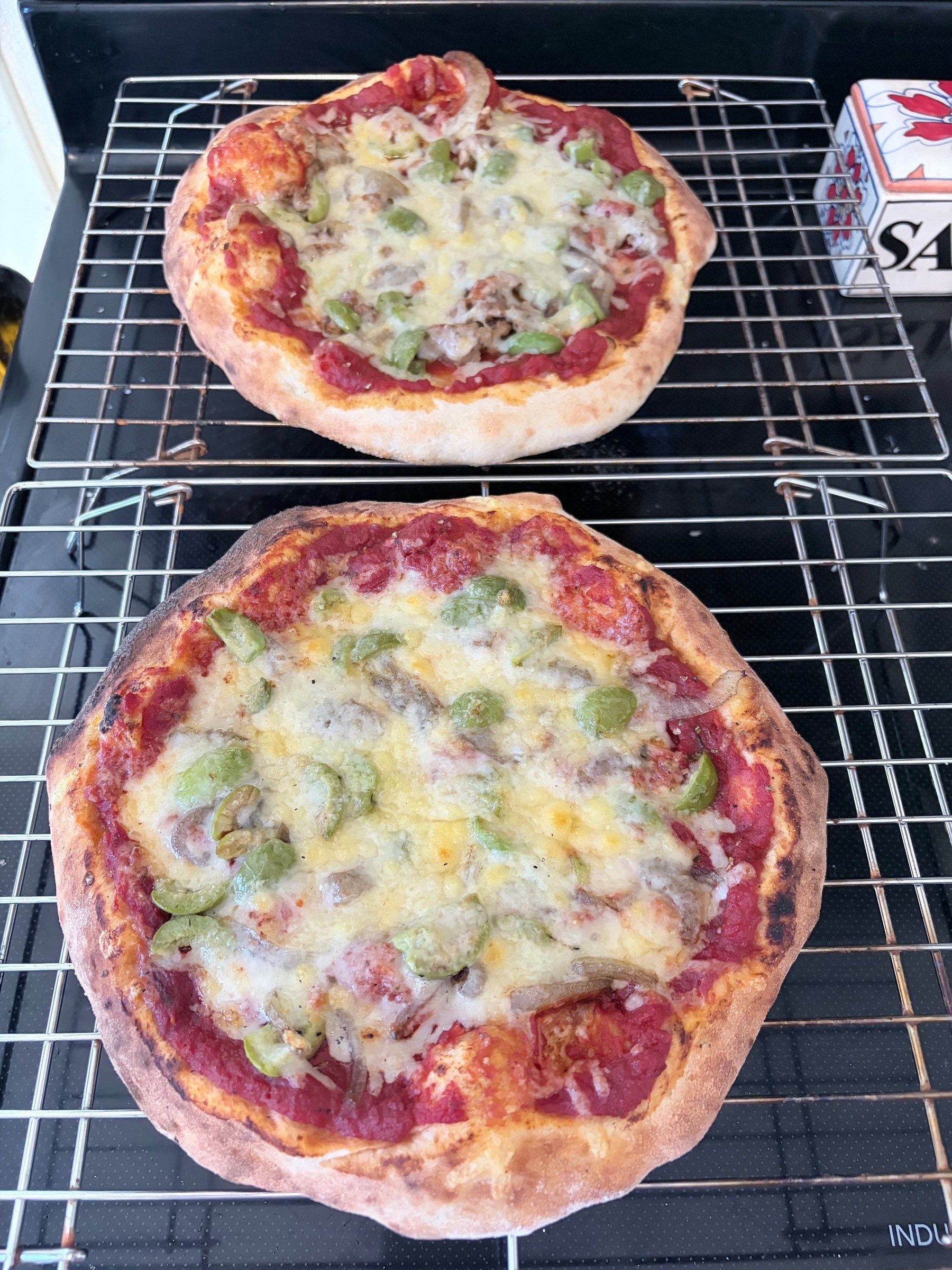 Two small pizzas sitting on wire cooling racks on top of a black glass stove top.