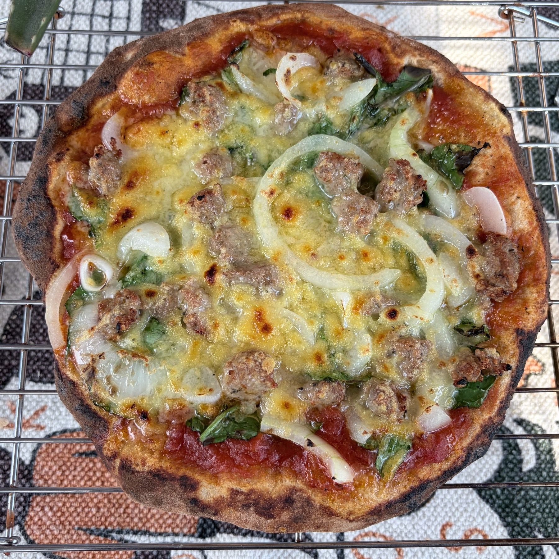 Small pizza on a cooling rack, sitting on a table with an illustrated white tablecloth.